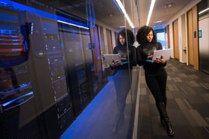 A woman with black dress working on a laptop leaning on a wall
