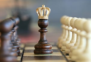 A chess pawn with crown on its head with other chess pawns at the side
